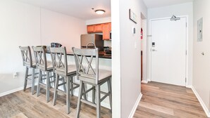 A modern kitchen with wooden cabinets and a dining area with four wooden chairs. - Bright 2BR Retreat w/ Pool – 1.5 Blocks to Oceanfront & Boardwalk (Virginia Beach)