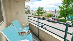 A balcony with two blue chairs, a view of a parking lot, and buildings in the background. - Bright 2BR Retreat w/ Pool – 1.5 Blocks to Oceanfront & Boardwalk (Virginia Beach)