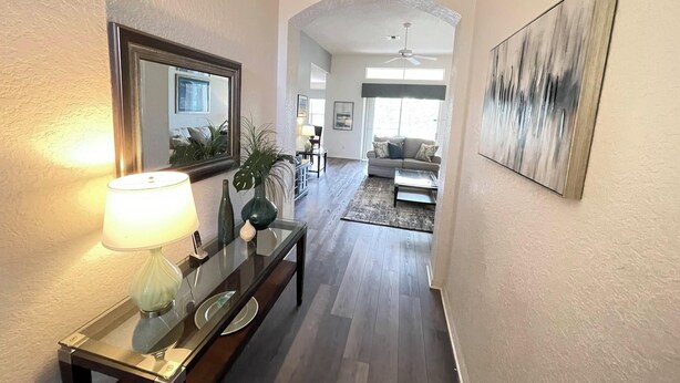 A hallway with a glass-top table, a lamp, and a mirror. There is a sofa and a painting in the background. - 4BR Villa Bright and Spacious w/ Pool (Davenport)