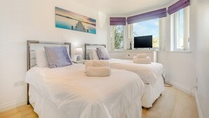 Quarto de hotel com duas camas, um quadro, uma televisão e uma janela com cortinas.