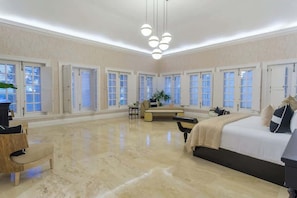 A spacious bedroom with a large bed, a seating area, and multiple windows.