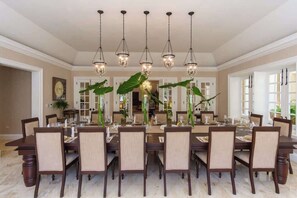 A formal dining room with a long table, multiple chairs, and hanging light fixtures.