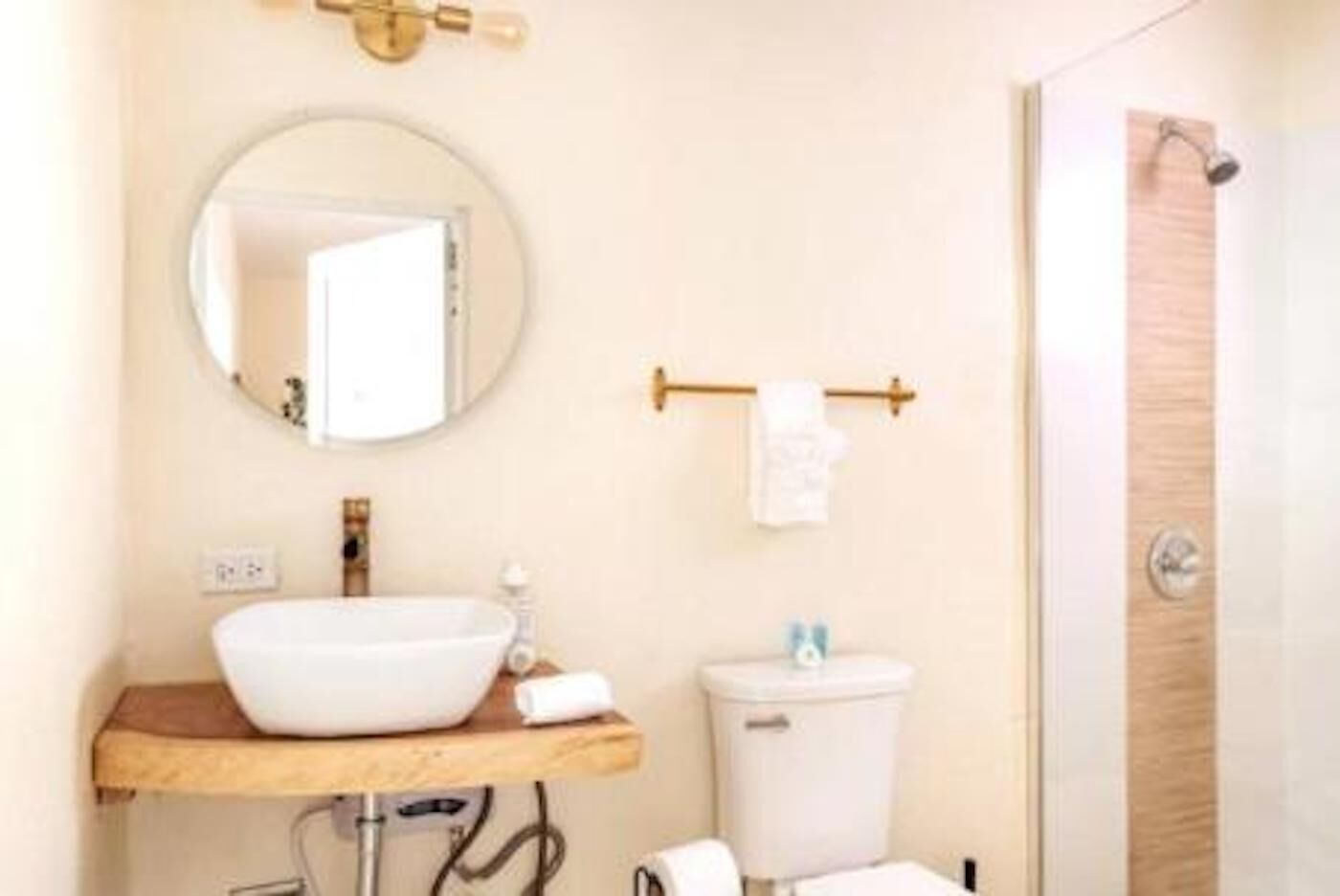 Een badkamer met een ronde spiegel, een houten wastafelmeubel, een witte wasbak, een toilet en een handdoekhouder.