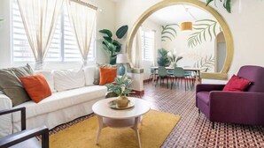 A modern living room with a white sofa, a purple armchair, and a round table. There is a large mirror on the wall and a dining area in the background. - 610atMiramar (San Juan)