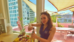 A woman at a table with a bottle of alcohol, a tray of food, and a window with a view of buildings. - 610atMiramar (San Juan)