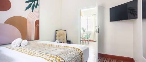 A hotel room with a bed, a TV mounted on the wall, and a view of the outside.