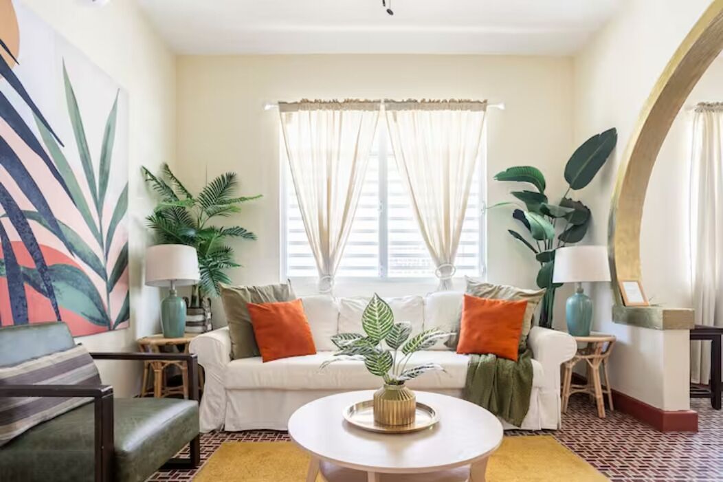 A living room with a white sofa, two side tables with lamps, a coffee table, and large green plants.