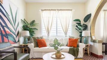 A living room with a white sofa, two side tables with lamps, a coffee table, and large green plants.