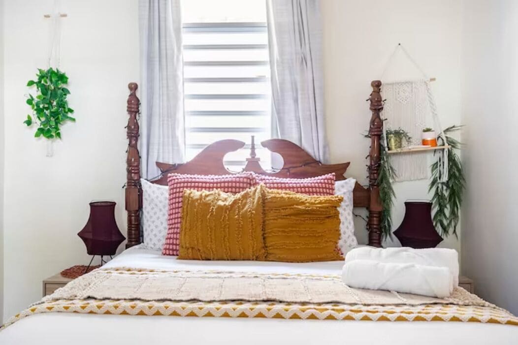A neatly made bed with a wooden headboard, a bedside lamp, and a macrame shelf with plants.