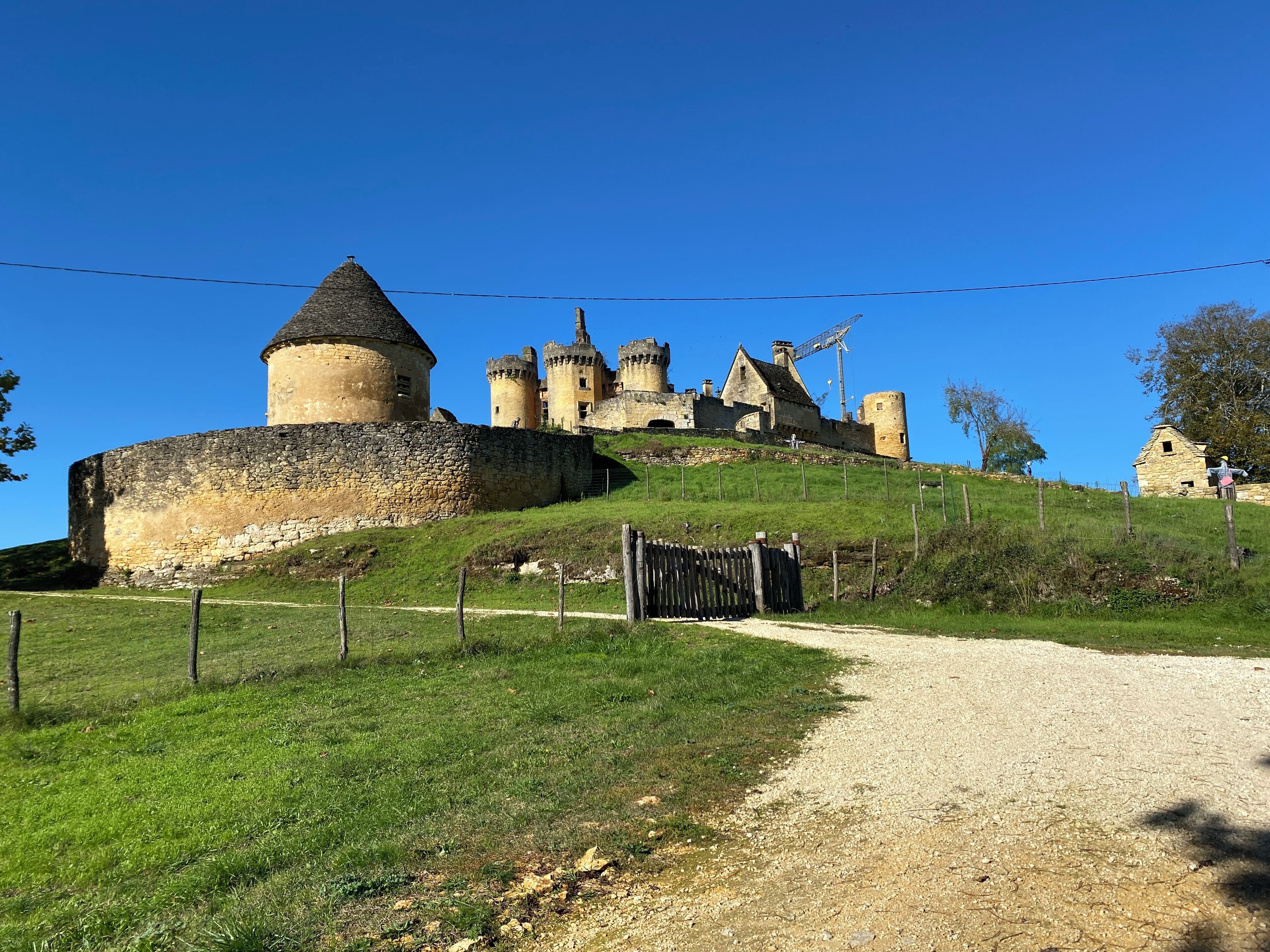 A historic castle with a round tower and multiple towers, surrounded by a stone wall and grassy terrain.