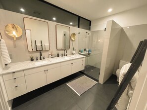 A modern bathroom with a double sink vanity, large mirrors, a glass shower enclosure, and a dark floor. - The Austin Oasis: Modern, spacious, and close to everything (Austin)