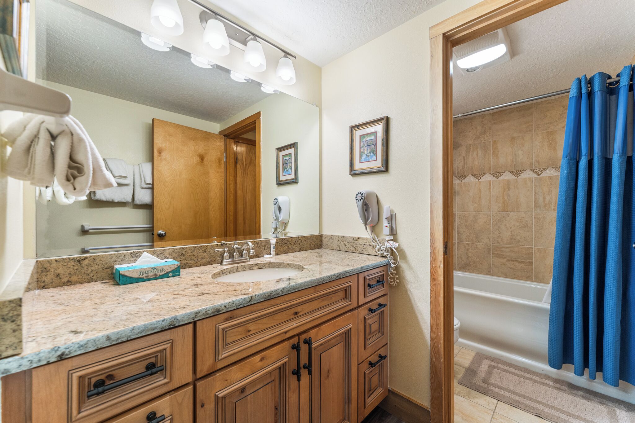 A bathroom with a double sink, wooden cabinets, a large mirror, and a shower with a blue curtain.