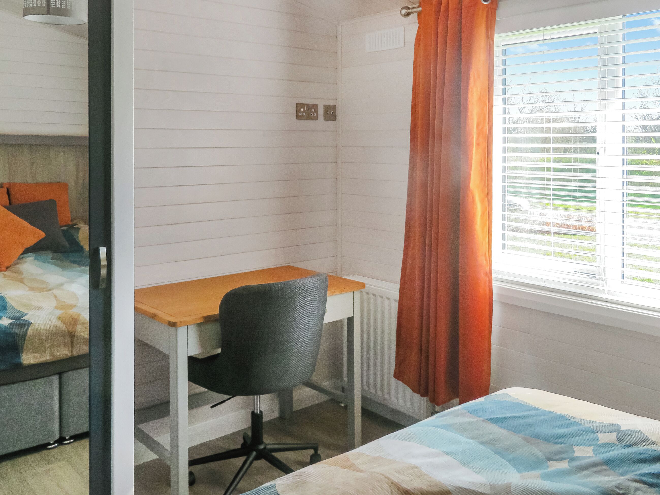 A bedroom with a bed, a desk, and a chair. There is a window with blinds and a curtain.