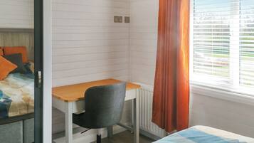 A bedroom with a bed, a desk, and a chair. There is a window with blinds and a curtain.