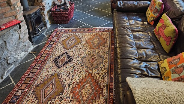Un salon chaleureux avec une cheminée en pierre, un tapis à motifs, un canapé en cuir agrémenté de coussins colorés et un mur en pierre.