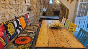 Une table en bois, avec un saladier au centre, est entourée de chaises aux couleurs vives. Un banc agrémenté de coussins à motifs est adossé au mur.