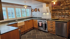 Une cuisine moderne avec un sol en pierre, des meubles en bois, une cuisinière en acier inoxydable et un four encastré.