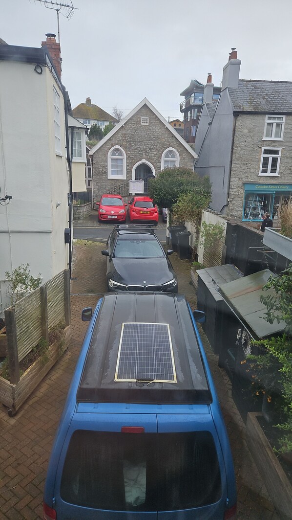 A street view with parked cars, a stone building with a sign, and a blue car with a solar panel.