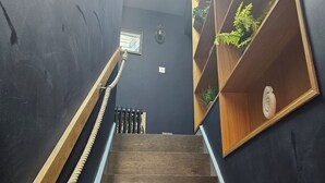 Un escalier en bois avec une rampe en corde, une lucarne et des étagères en bois ornées de plantes.