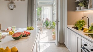A modern kitchen with a central island, a clock on the wall, and a view through an archway to a garden. - Villa Sunkiss Winery (Montecarlo)