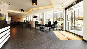 A modern hotel lobby with a reception desk, seating area, and large windows. - The Whitechapel (London)