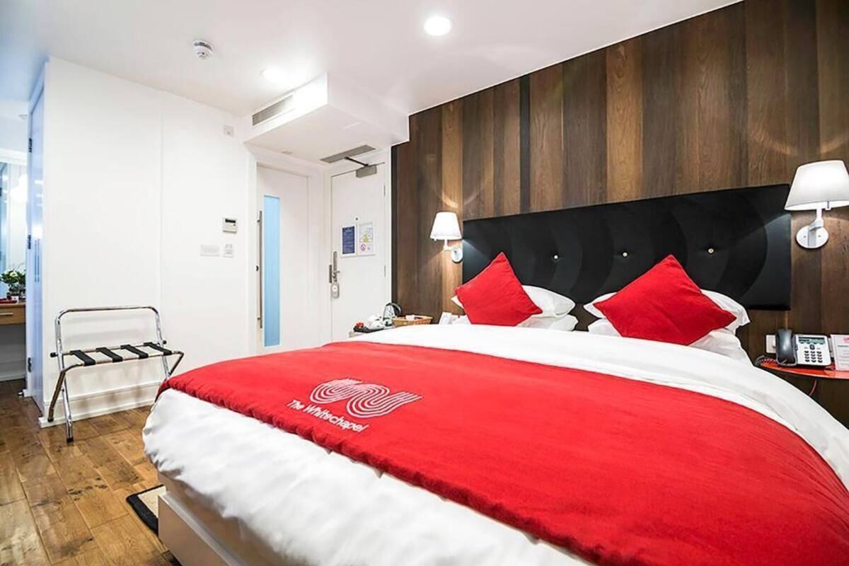 A hotel room with a large bed, a wooden headboard, two bedside lamps, and a red and white bedspread.