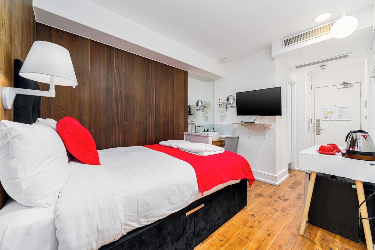 A modern hotel room with a large bed, a desk, a TV, and a mirror.