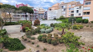 A residential area with multi-story buildings, a well-maintained garden with various shrubs and a palm tree, and a clear sky.