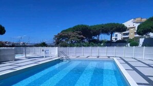 A rectangular swimming pool with clear blue water, surrounded by a white fence and a tiled deck.