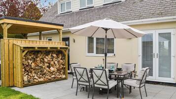 En patio med et træbeklædt pergola, et bord med stole og en stabel brænde.
