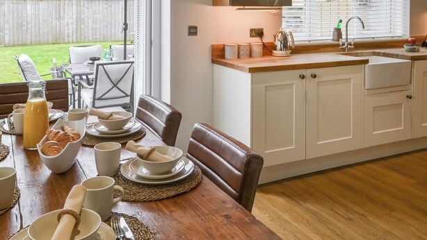 Un comedor con una mesa de madera dispuesta para el desayuno, incluyendo cruasanes, tazas de café y una botella de jugo.