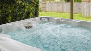 Un jacuzzi con caída de agua, rodeado por una terraza de madera y abundante vegetación.