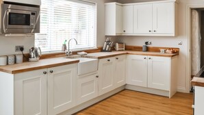 Una cocina moderna con armarios blancos, microondas integrado, un lavamanos y una ventana con persianas.
