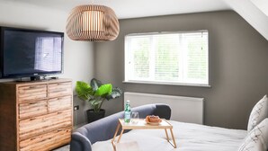 Un dormitorio moderno con cama, televisión, cómoda de madera, planta y ventana con persianas.
