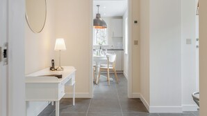 Un pasillo que conduce a una cocina con armarios blancos, una mesa de comedor, sillas y una lámpara colgante.