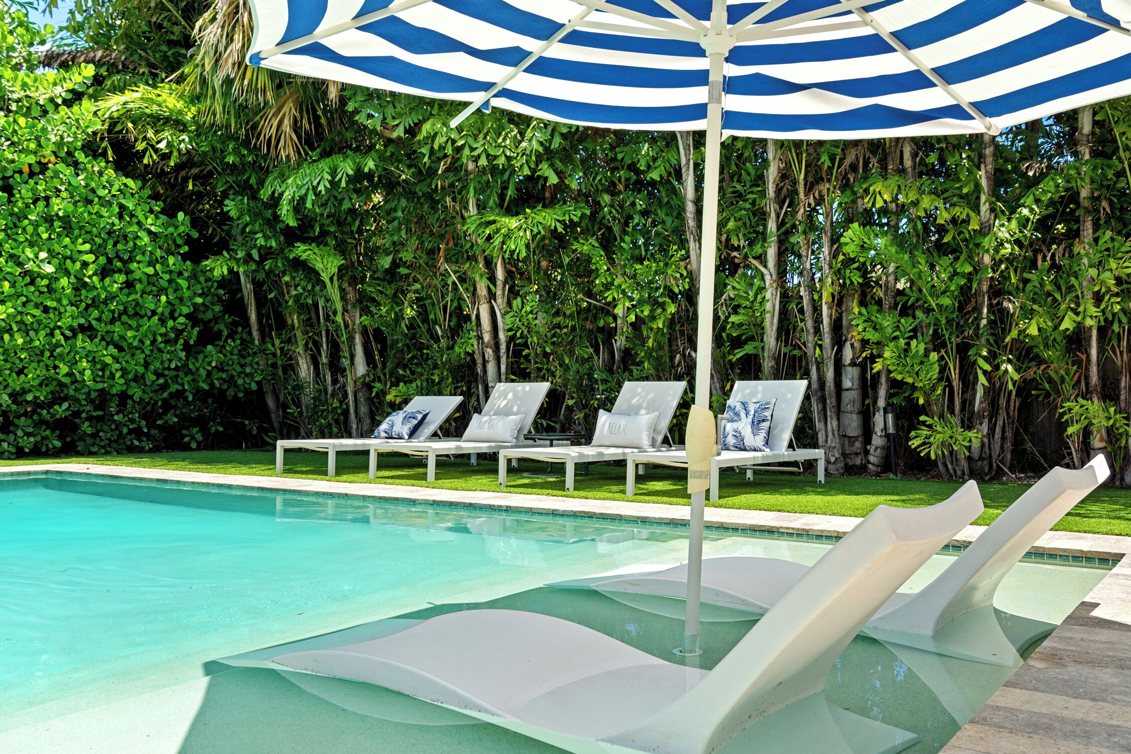 A swimming pool with lounge chairs and a striped umbrella.