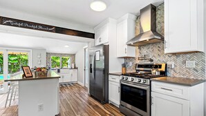 A modern kitchen with white cabinets, a stainless steel refrigerator, a gas stove, and a herringbone-patterned backsplash. - Sep Discount! Heated Pool, Close to Atlantic (Delray Beach)