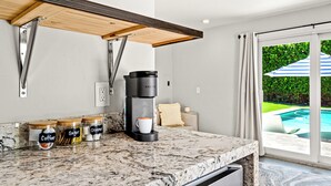 A kitchen with a coffee maker, sugar, and creamer jars on the counter, and a view of a swimming pool through a glass door. - Sep Discount! Heated Pool, Close to Atlantic (Delray Beach)