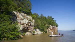 Um barco em um rio calmo, com penhascos rochosos e vegetação densa nas margens.