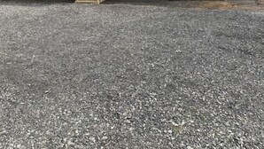 Um edifício térreo com varanda frontal, uma pequena escadaria e um caminho de entrada de brita.