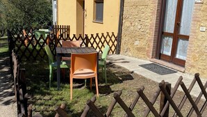 Un espace extérieur aménagé dans un style rustique, avec une table et des chaises en bois, une petite fenêtre et un mur en pierre.