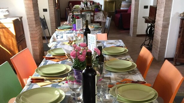 Une longue table à manger, dressée avec de la vaisselle verte, des verres à vin et des couverts, entourée de chaises orange.