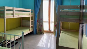 Une chambre avec des lits superposés, une fenêtre avec des rideaux et un téléviseur fixé au mur.