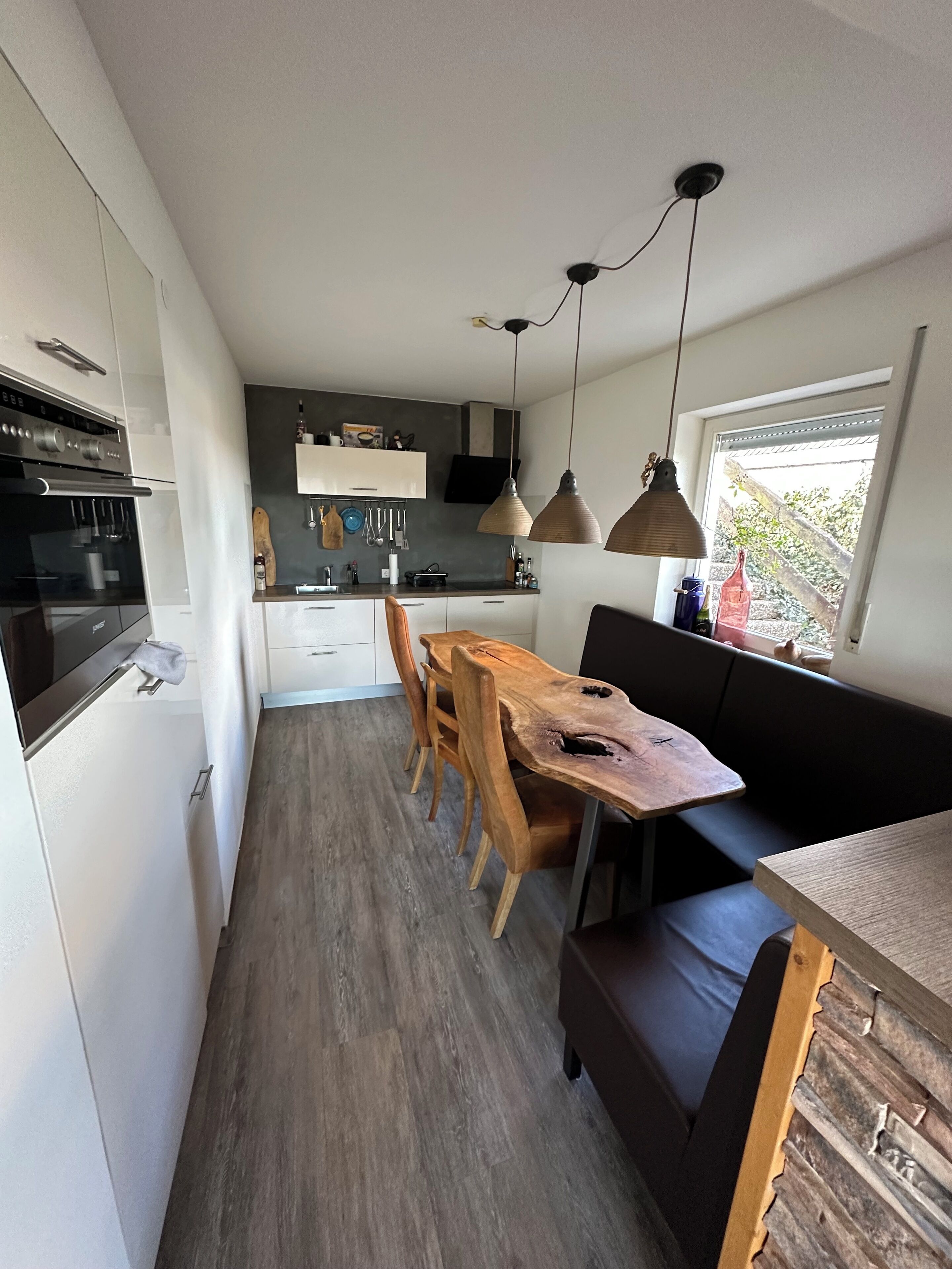 Una cocina compacta con electrodomésticos modernos, un comedor con sillas de madera y un banco empotrado.