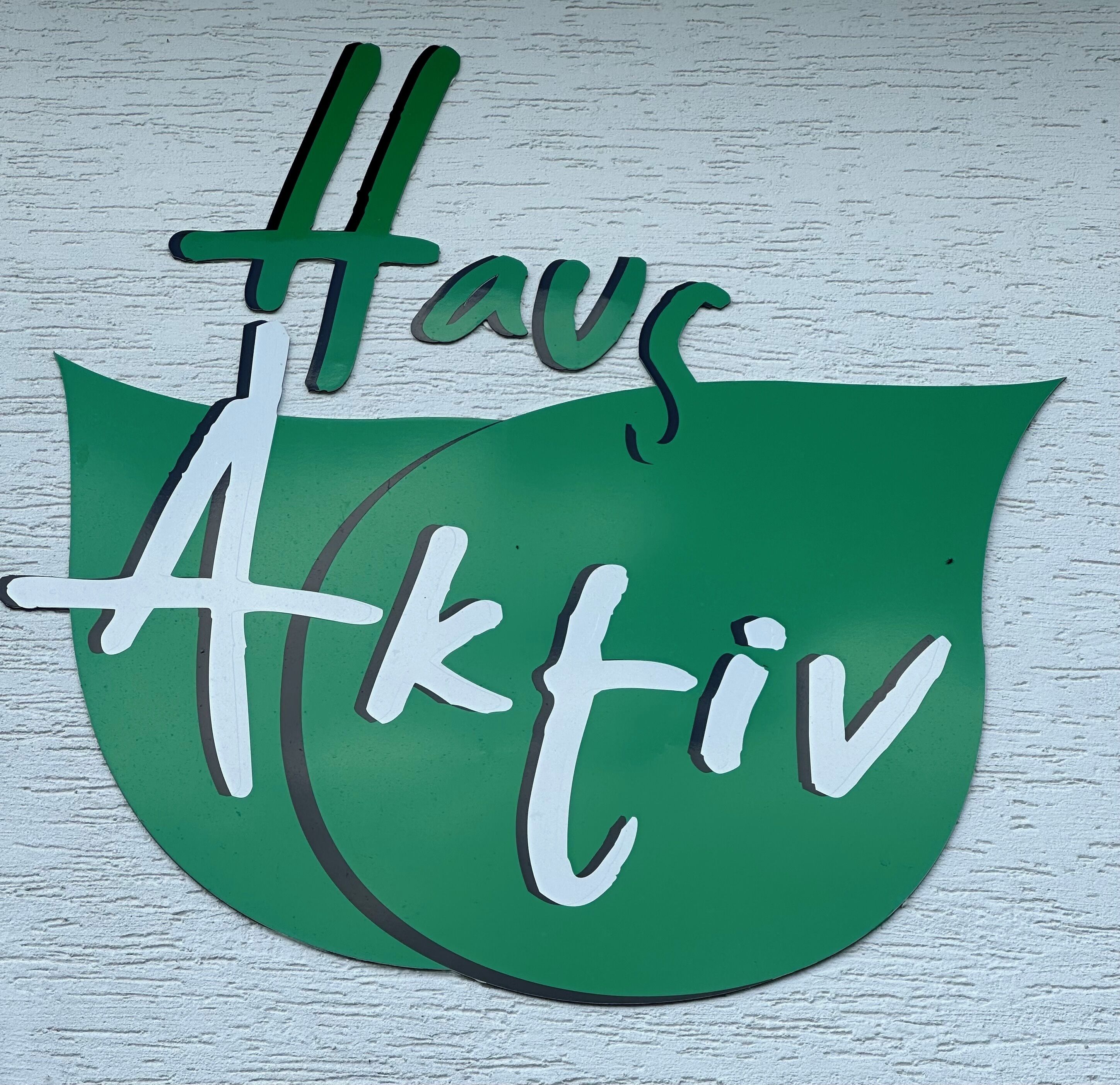 A green leaf-shaped sign with the text "Havas Aktiv" on a white textured wall.