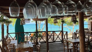 Una terraza de madera al aire libre con mesas y sillas, con vista a la playa.