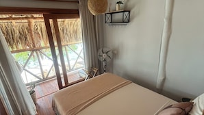 Un dormitorio con cama, ventilador, lámpara colgante, ventana con cortinas y vista al exterior.