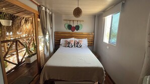 Un dormitorio con cabecera de madera, cama con ropa de cama blanca, lámpara colgante y ventana con vista a árboles.