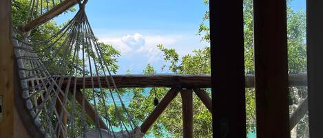 A hammock chair attached to a wooden structure overlooking a beach with clear skies and calm waters.