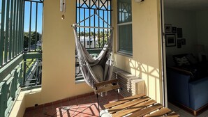 Un balcón con una silla hamaca, una mesa de madera y vistas al exterior.